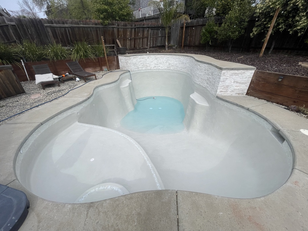 Same pool after renovation with fresh gray plaster and new stacked stone wall