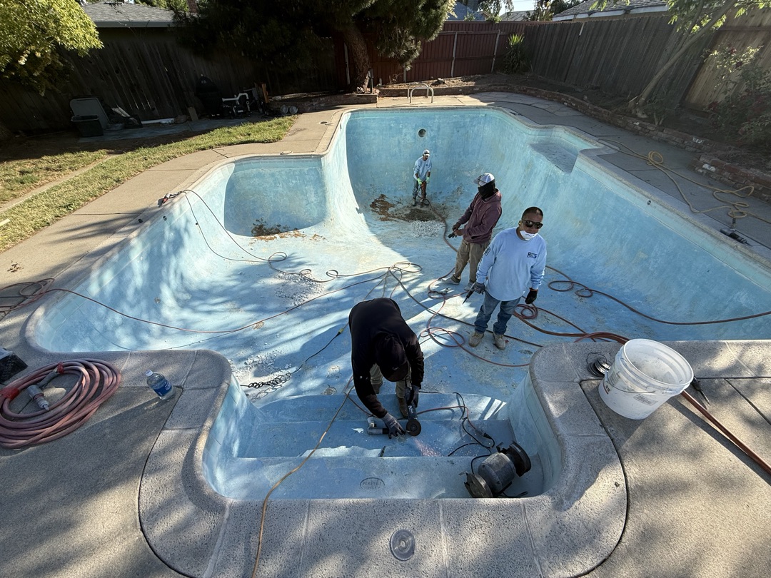 Crew chipping out old worn blue plaster from pool before replaster
