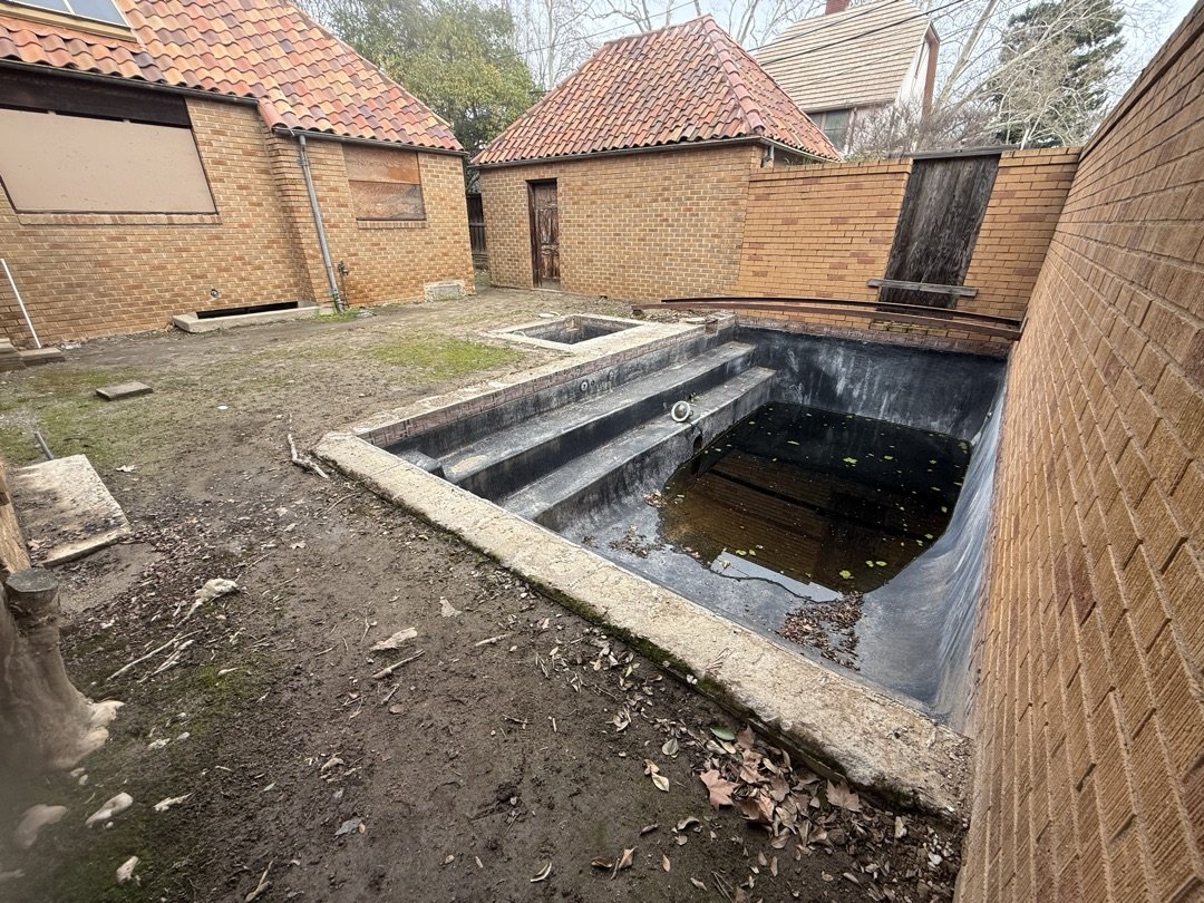 Empty drained pool with old spa and dirt yard before total backyard reset